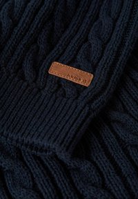 Suéter de punto en un oscuro navy con un patrón de punto de cable, puños de canalé y una etiqueta de cuero marrón con el texto "name it."