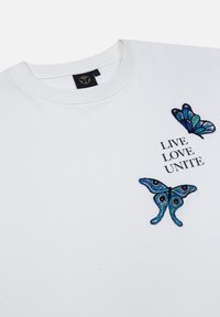 Witte sweatshirt met twee blauwe geborduurde vlinderontwerpen. Tekst "LIVE LOVE UNITE" in zwart. Ronde hals, relaxte pasvorm.