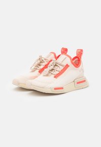 Beige athletic shoes with coral accents, textured upper, elastic laces, and a padded collar. Features a patterned sole and branding on the heel.