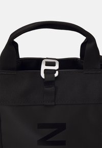 Sac en tissu noir avec des poignées courtes et une fermeture à boucle argentée sur le dessus, avec une grande lettre noire Z à l'avant.