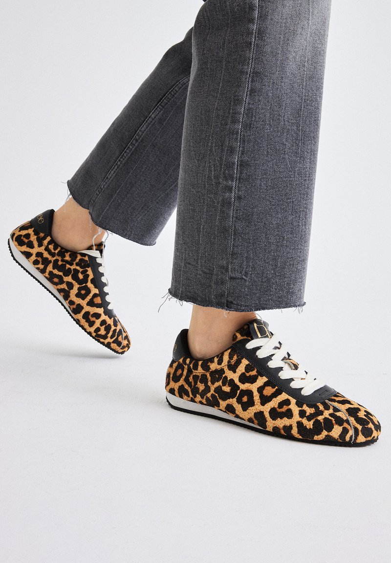 Las zapatillas de leopardo presentan un material texturizado suave con acentos en negro, cierre de cordones y una suela de goma de perfil bajo.
