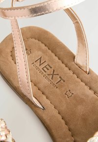Hele pruun nubukist sandaal, millel on roosa metallist rihm ja reljeefne "NEXT Forever Comfort" brändimine jalanõu sisemuses.