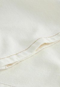 Light beige fabric with a textured finish, featuring contrasting brown stitching along the edge of a folded area.