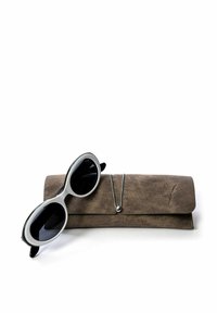 Mustat aurinkolasit, joissa on ylisuurikokoiset soikeat kehykset ja tummat linssit, lepäävät teksturoidun ruskean nahkakotelon päällä, jossa on metallinen sulkumekanismi.