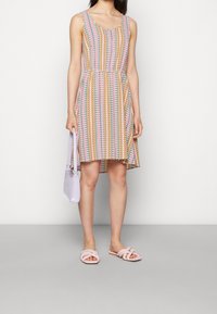 Vestido sin mangas, colorido y estampado, con diseños en zigzag en rosa, amarillo y azul, ajustado en la cintura, combinado con sandalias rosas de tira y un bolso lila.