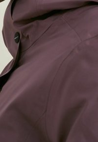 Fioletowa wodoodporna kurtka z wysokim kołnierzem, zapięciem na napy i gładką teksturą, z widocznymi szwami i dopasowanym krojem.