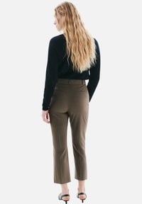 Pantalons marron ajustés avec une coupe droite, deux poches arrière et une texture de tissu lisse. Assortis à un haut noir à manches longues.