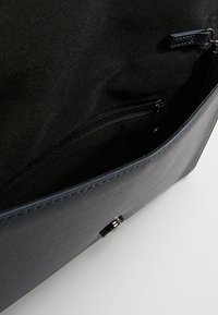 Mörkblå strukturerad läderväska med svart tygfoder och en zippered ficka för säker förvaring. Metalliska detaljer som accent.