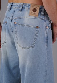 Helle blaue Denim-Jeans mit einem verblassten Finish. Zu den Besonderheiten gehören Kupferriegel, zwei Gesäßtaschen und ein tanfarbenes Lederpatch mit Branding.