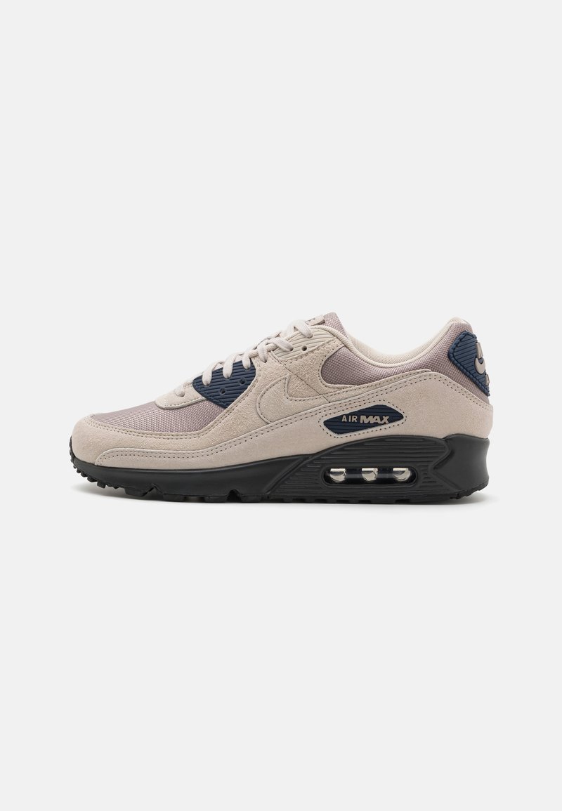 Beige semskinn og mesh sneakers med marineblå detaljer, svart såle, synlig Air Max demping, og beige snøringer. Rund tå og polstret krage.
