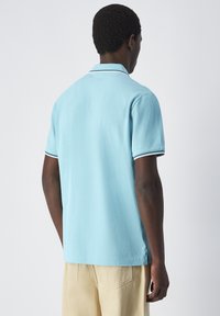 Jasnoniebieska koszulka polo wykonana z bawełny; krótkie rękawy z ribbowanym kołnierzykiem i kontrastującymi białymi paskami. Prosty design, luźny krój.