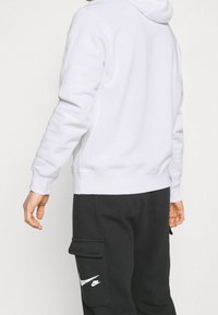 Vit luvtröja med huva och slät textur, med en känguruficka och ribbade muddar, kombinerad med svarta cargobyxor med en logotyp.