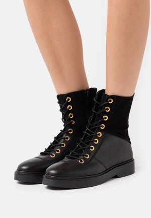 Black leather and suede lace-up ankle boots with gold eyelets, padded collar, and rubber sole. Features a side zipper for easy wear.