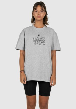 Gray oversized t-shirt featuring a graphic print in black. Short sleeves, round neckline, paired with black leggings. Soft cotton texture.