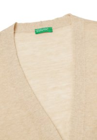 Beżowy kardigan w dekolcie w serek, wykonany z miękkiego materiału. Posiada subtelną fakturę oraz zieloną metkę marki przy dekolcie.