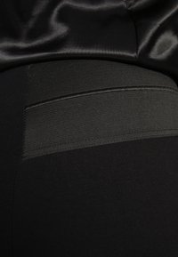 Leggings noirs avec une texture lisse et douce, dotés d'une bande côtelée contrastante à la taille. Le tissu est léger et extensible.
