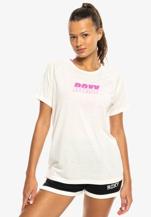 Bílý krátký rukáv T-tričko s růžovou grafikou "ROXY", spárované s černými šortkami s bílým lemem a brandingem "ROXY" na boku.