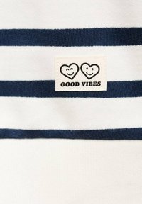 Tessuto bianco con strisce orizzontali blu navy presenta un'etichetta tessuta con due cuori e il testo "GOOD VIBES" sotto in nero.
