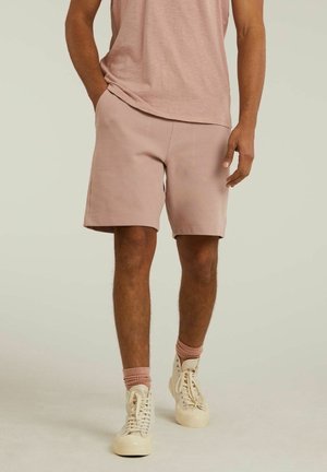 Lys rosa shorts lavet af blødt stof, med en afslappet pasform, sidelommer og syede detaljer. Sammen med beige sneakers og pink sokker.
