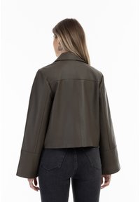 Grüne Leder-Cropped-Jacke mit Reverskragen, ausstellenden Ärmeln und glatter Textur, von hinten mit dunklen Jeans präsentiert.