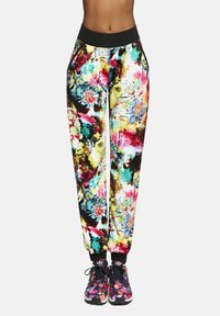 Wielokolorowe kwieciste joggery z czarną elastyczną talią, o błyszczącej powierzchni i zwężanych mankietach. W połączeniu z wzorzystymi czarnymi sportowymi butami.