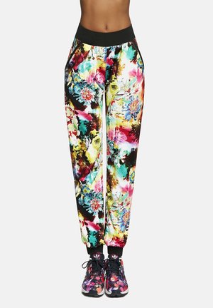 Wielokolorowe kwieciste joggery z czarną elastyczną talią, o błyszczącej powierzchni i zwężanych mankietach. W połączeniu z wzorzystymi czarnymi sportowymi butami.