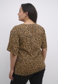 Blouse en bronze à imprimé léopard avec des manches courtes, fermeture en goutte d'eau à l'arrière et coupe décontractée. Tissu doux avec une texture lisse.