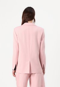 Blazer rose clair à coupe slim, avec une fente dans le dos et des accents noirs aux poignets. Confectionné dans un tissu lisse, design ajusté.
