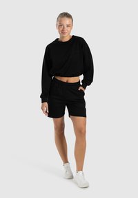 Schwarzer, verkürzter Sweatshirt und passende Shorts aus weichem Material. Der Pullover hat einen runden Ausschnitt; die Shorts verfügen über einen elastischen Bund.