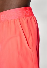 Coral shorts with a fitted waistband labeled "BORG." Features side pockets and smooth, lightweight fabric with subtle texture.