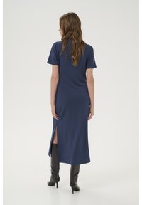 Navy blue midi dress with short sleeves, side slits, and smooth texture. Worn with knee-high black boots.