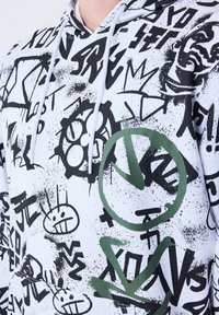 Sudadera con capucha que presenta una tela blanca con patrones de graffiti en negro y verde, incluidas formas abstractas y caras sonrientes.
