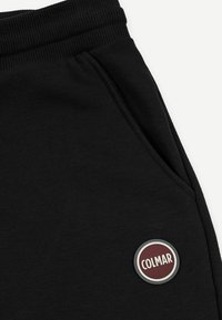 Pantaloni della tuta neri con una fascia in costina in vita, dotati di una tasca laterale e una toppa rotonda del logo Colmar in bordeaux e bianco. Texture liscia.