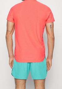 Camiseta deportiva de manga corta en color coral con un acabado texturizado, combinada con pantalones cortos de color azul claro, que cuentan con aberturas laterales para mayor movilidad.