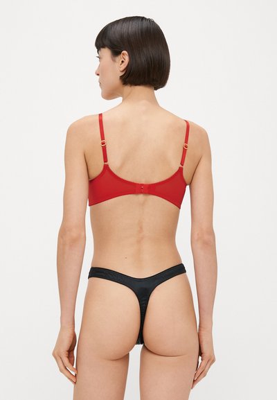 Sarkans krūšturis ar regulējamām lencēm un zelta elementiem, komplektā ar melnu tangiem. Gluda auduma un minimālistisks dizains, izceļ vienkāršu siluetu.