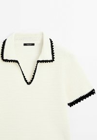 Polo à manches courtes en maille blanche avec bordure festonnée noire sur le col et les bords des manches, étiqueté Massimo Dutti.