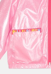 Růžová lesklá bunda s lesklou texturou, vybavená přední kapsou a barevně kontrastním štítkem "BUBBLELUSH". Zapínání na zip a elastické manžety.
