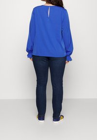 Top azul de manga larga con detalle de cut-out en la parte trasera, combinado con pantalones de mezclilla oscuros y zapatillas multicolores con rayas.