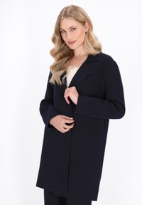Cappotto in misto lana blu navy con colletto a revers, maniche lunghe e design minimalista. Presenta una linea dritta e una morbida trama.