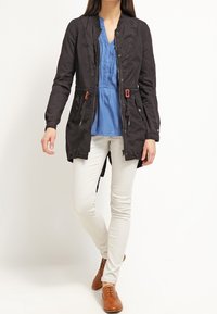 Czarna, lekka kurtka z zapięciem na guziki, dwoma przednimi kieszeniami i detalami w postaci sznurka. Nosił ją na niebieskiej bluzce i białych spodniach. Brązowe buty.