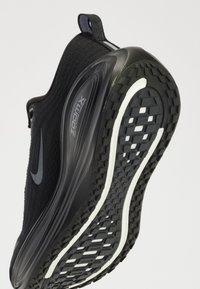 Chaussure de running noire Nike inclinée pour montrer la semelle texturée avec des accents blancs et un amorti ZoomX visible dans la semelle intermédiaire.