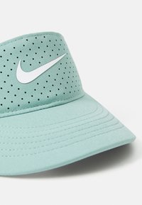 Hellgrüner Nike-Visor aus atmungsaktivem Material, mit Perforation, gebogenem Schirm und prominentem weißen Swoosh-Logo.