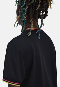 Camisa polo negra con un tejido texturizado, con acentos coloridos en rosa y verde a lo largo del cuello y los extremos de las mangas.