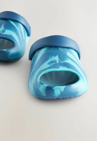 Sinikuvioiset liukurit avonaisella varvassyydellä, joissa on tukeva sininen remmi ja sileä pinta. Kevyt ja rento tyyli.