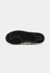 Sneaker sole, black rubber with zigzag traction pattern. Beige midsole with three white stripes. Smooth texture with contrast detailing.