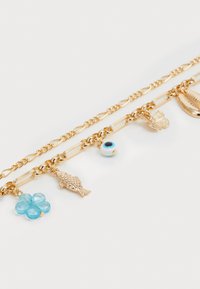Gouden armband met bedels, voorzien van een bloemige blauwe kraal, vissen, vlinders en oogvormige bedels op schakels en kettingsegmenten.