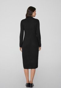 Schwarzes, geripptes Midi-Kleid mit langen Ärmeln, hohem Kragen und figurbetonter Silhouette. Entworfen mit einer glatten Textur und minimalistischem Stil.