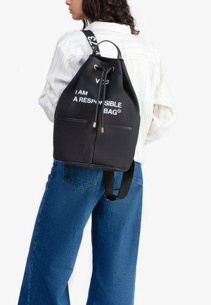 Mochila de lona negra con cierre de cordón, herrajes en tono dorado, bolsillos frontales y texto blanco que dice "SOY UNA MOCHILA RESPONSABLE."