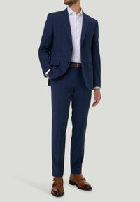Marineblauer maßgeschneiderter Anzug mit Reverskragen, strukturiertem Stoff und passender Hose. Getragen mit einem weißen Hemd und braunen Lederschuhen.