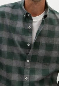 Grün und grau karierter Hemd mit Button-Down-Kragen. Verfügt über eine Brusttasche und weiße Knöpfe auf einem weichen Stoff.